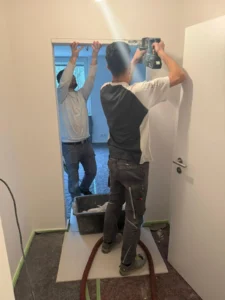 Handwerker installieren Türrahmen mit Elektrowerkzeug, Raum im Umbau, Boden abgedeckt.