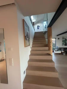 Holztreppe mit Glasgeländer, Bilder an der Wand, moderner und offener Raum.