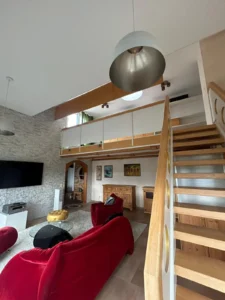 Modernes Wohnzimmer mit Galerie, roter Sitzgruppe, Holzwendeltreppe, Glastisch, Steinwand-TV.