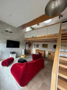 Wohnzimmer mit modernem Design, rotem Sofa, Sessel, gläsernem Tisch und großer Wand-TV.