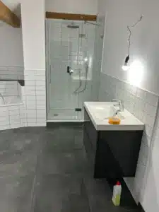 Modernes Badezimmer mit Dusche, Glasabtrennung, weißen Fliesen und schwarzem Waschbeckenunterschrank.