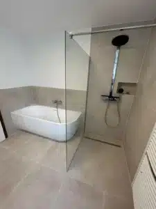 Modernes Badezimmer mit freistehender Wanne und Dusche, Glaswand, helle Fliesen.