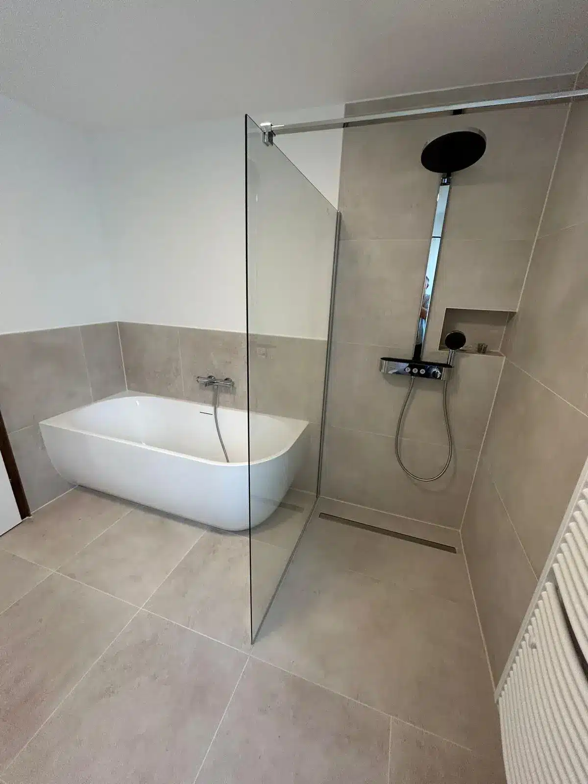 Modernes Bad mit freistehender Wanne, begehbarer Dusche und großen beigen Fliesen.