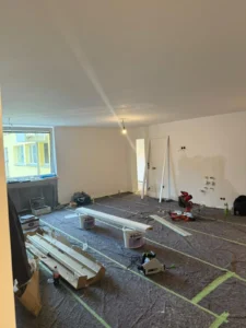 Raumrenovierung mit Abdeckplanen, Werkzeugen und Materialien, Tageslicht durch Fenster.