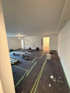 Renovierungsraum mit weiß gestrichenen Wänden, abgedecktem Boden und verstreuten Werkzeugen.