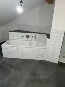 Badezimmer mit weißer Eckbadewanne, Fliesenwänden und dunkelgrauem Boden.